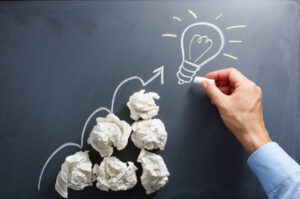 Drawing light bulb on blackboard. Many paper balls.